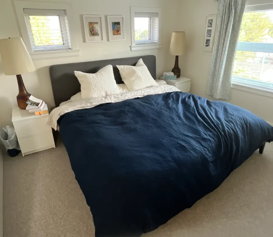 David's bedroom after: a navy duvet, white pillows and clear nightstands with lamps